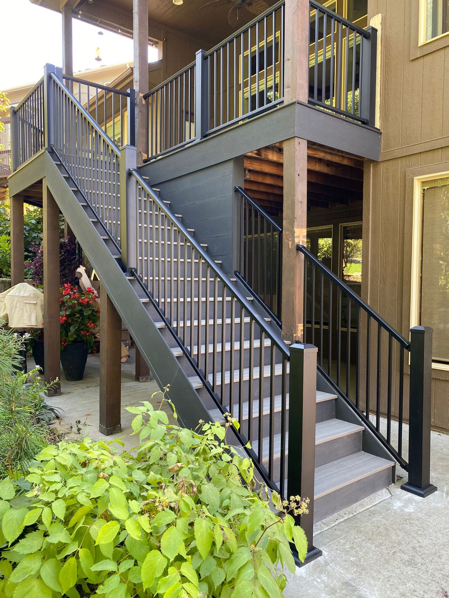 Two-story deck stairs with black railing beside a landscaped patio