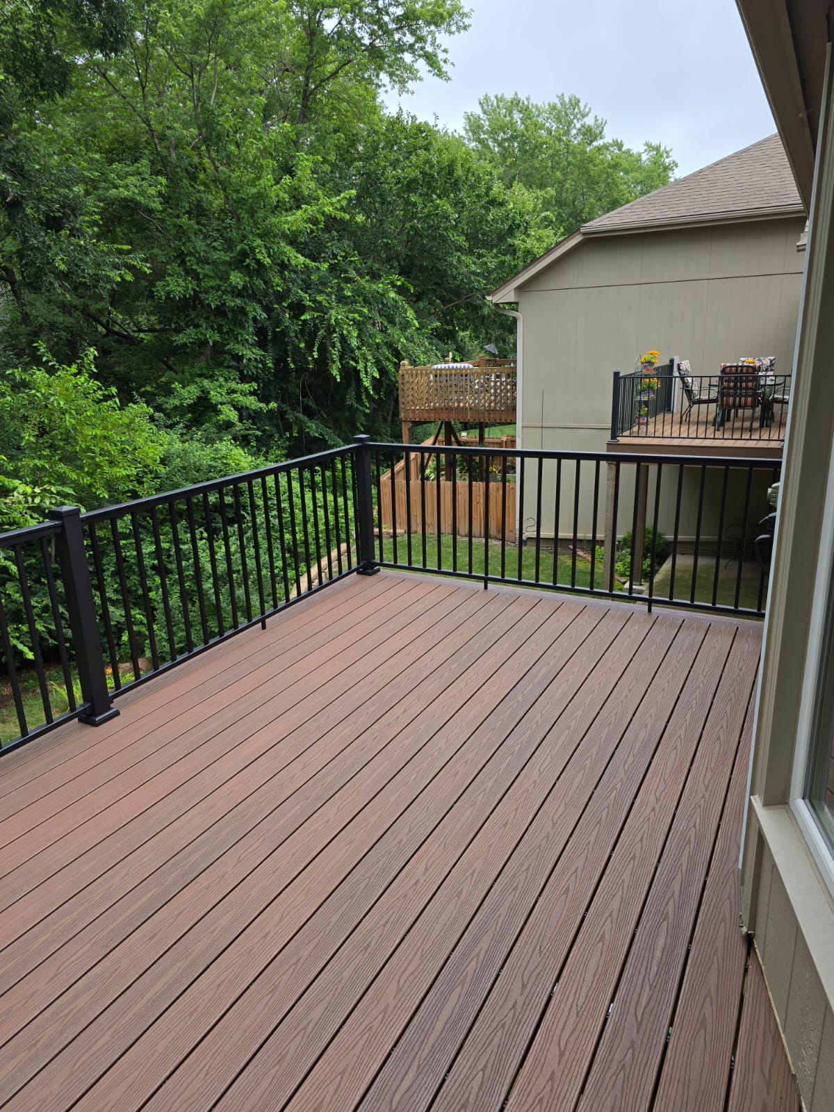 Brown composite deck with black aluminum railing and treed backyard